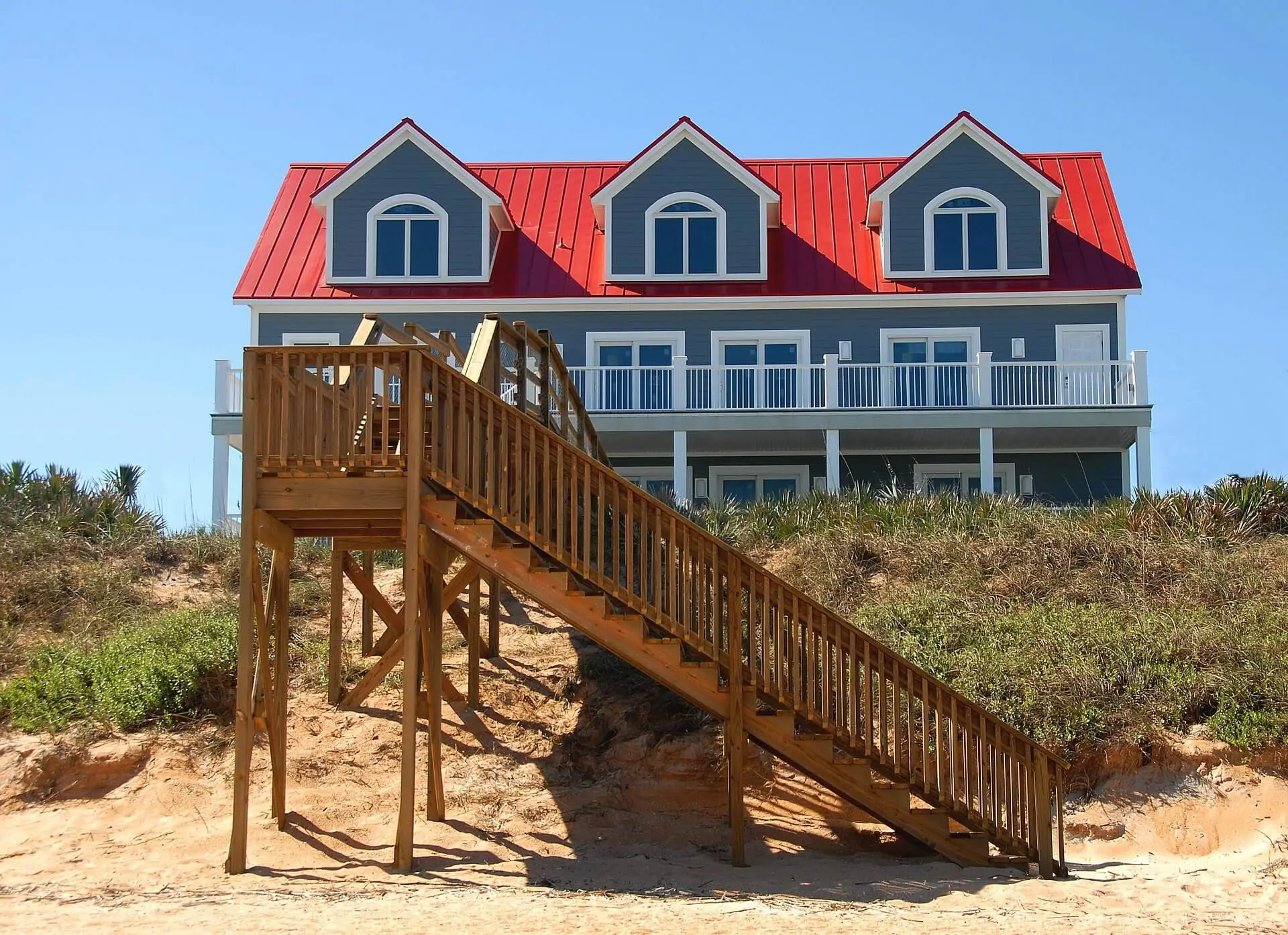 Immobilienkauf im Ausland: Strandhaus auf Stelzen mit Holzsteg durch die Dünen